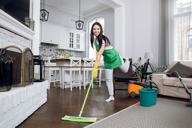 Young attractive cheerful brunette woman, professional worker of cleaning service, having fun while washing floor when cleaning up luxury appartment.